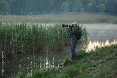 Photos A photographer in a green jacket and cap uses a large telephoto lens to capture