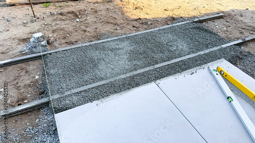 Construction site showing freshly poured concrete slab with gravel base and leveling tool 