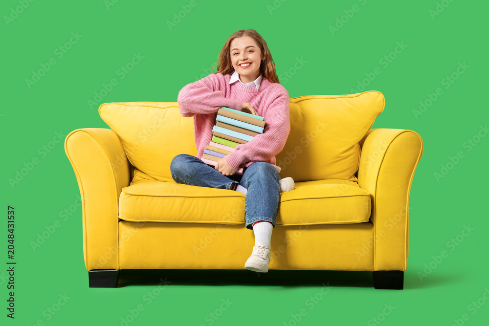 Obraz premium Young woman with stack of books sitting on sofa against green background