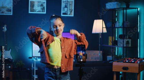 Photos Joyful kid dancing in dimly lit home studio interior, producing content for online channel with smartphone on tripod