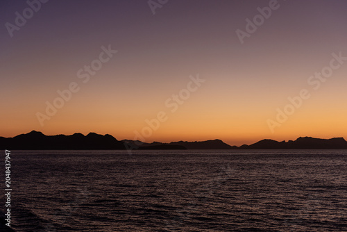 Sunset across the sea, coastline stretching into the distance.