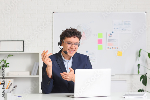 Young male online business consultant with headset and laptop video chatting ...
