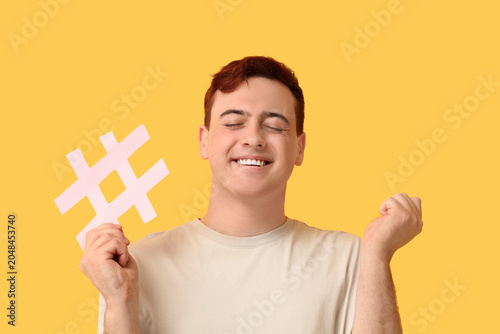 Happy young man with hashtag sign on yellow background