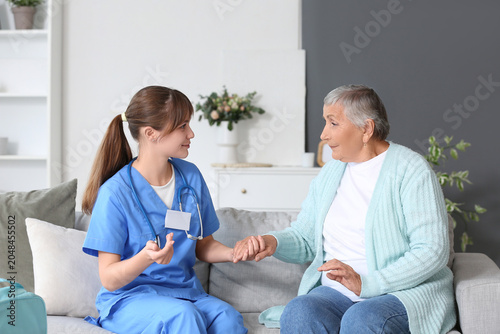 Senior woman with caregiver holding hands at home