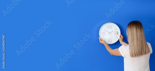 Woman hanging clock on blue...