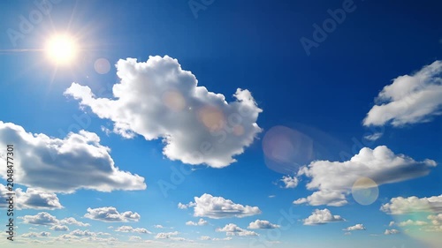 Bright sun in deep blue sky with scattered white cumulus clouds and lens flare