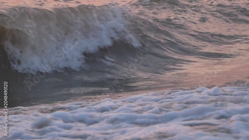 Close-up of a dynamic ocean wave splashing during sunset, capturing the warm golden reflection of the sun on the water surface.