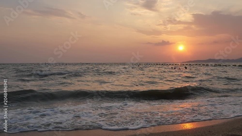 Beautiful golden hour sunset over a tropical beach with sea waves rolling onto the shore.
