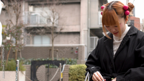 Tableau sur toile Young Japanese Woman in Black Coat Adjusting Her Belt in Harajuku