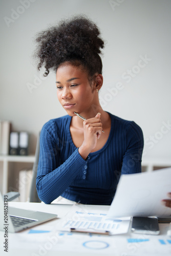 Young black businesswoman analyzing financial documents, thinking about strategy for business growth, making important decisions in a modern office setup