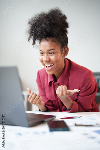 Obraz na plátně Black woman expressing excitement and celebrating success while looking at her l