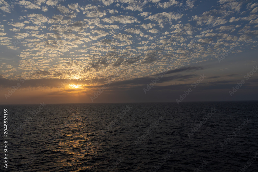 Obraz premium Sunset over open ocean with mackerel sky cloud formation and golden light reflection