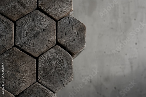 Macro Close-up of Geometric Stacked Weathered Hexagonal Timber Logs against Minimalist Industrial Concrete Background with Negative Space