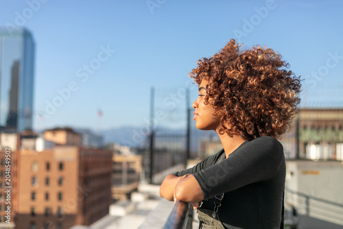 фотографія Person with curly hair gazes over a cityscape from a rooftop.