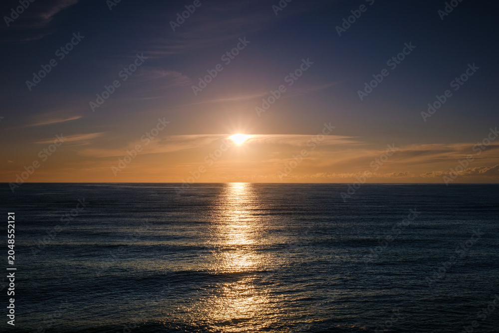 Fototapeta premium Beautiful golden sunset over the calm sea horizon with sun reflecting on water.