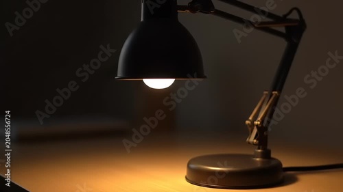 Turning on a desk lamp in a dark room for illumination.