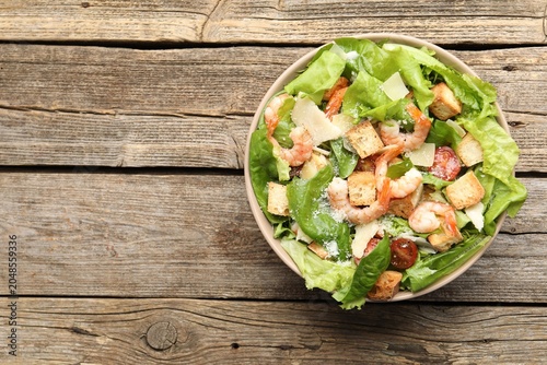Fotografie Delicious Caesar salad with shrimps in bowl on wooden table, top view