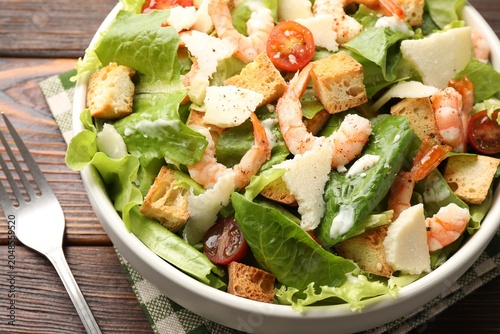 Photography Delicious Caesar salad with shrimps in bowl served on wooden table, closeup