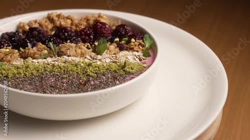 Colorful breakfast smoothie bowl with granola, blackberries, and chia seeds rotating on a plate, fa01