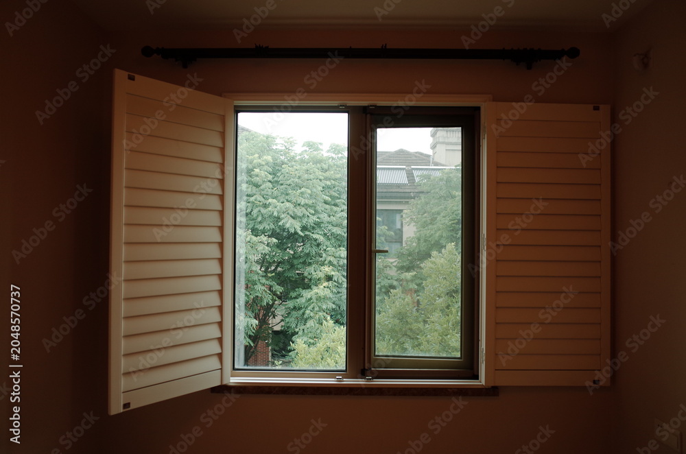 Fototapeta premium Open wooden shutters framing a view of green trees from an interior room
