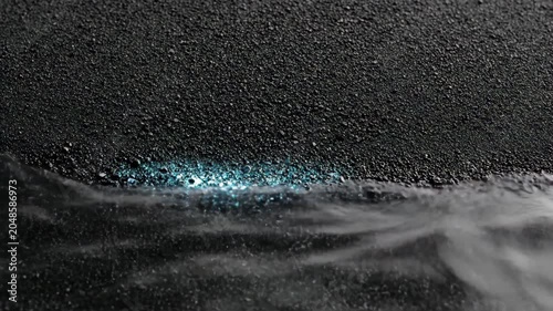 Bioluminescent waves washing onto dark volcanic sand shore. Night ocean water with blue glowing microorganisms hitting black beach. Marine nature phenomenon concept