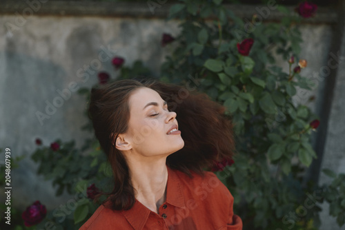 Obraz na plátně Young woman in an orange shirt enjoys a breezy moment among blooming roses, eyes