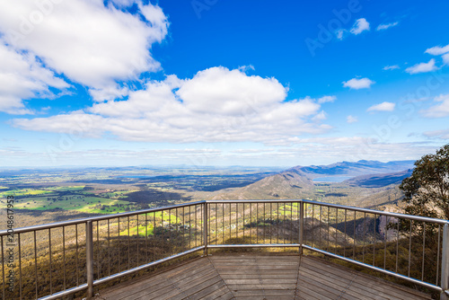 Lake Bellfield view from the Boroka Lookout balcony on a sunny day in the Grampians, Victoria, Australia. Blue sky and white clouds stretch above the reservoir and surrounding mountain ranges in brigh