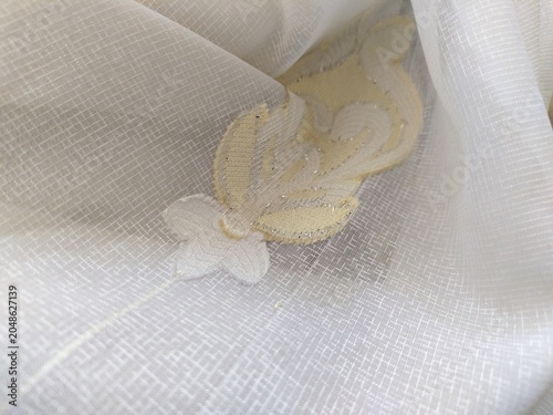 Closeup shot of white with golden flower ornament tulle netting curtain. Photo with shallow focus. 
