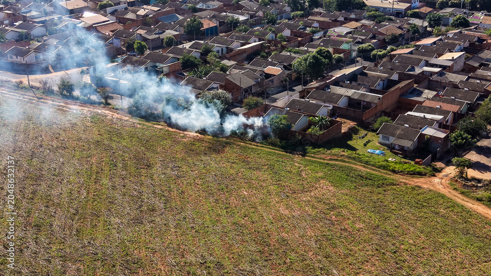 Fototapeta premium Aerial view of smoke rising from a field adjacent to a residential neighborhood with dense housing and tiled roofs