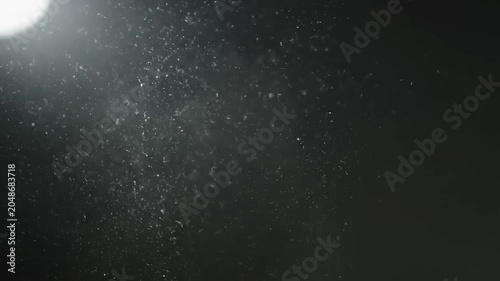 A stunning video captures a bright light shining against a dark background with small particles flying around.