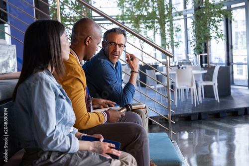 Diverse coworkers discussing and holding mic, phone with blue case, notepad in office lounge
