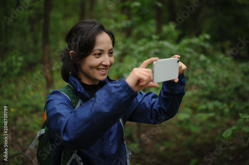 Cheerful asian traveler taking photo on smartphone in forest 