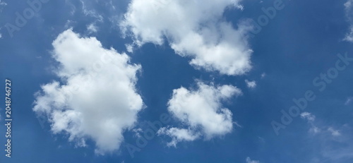 A bright blue sky with fluffy white clouds. The clouds resemble cotton balls or bushes scattered across the sky. Cumulus clouds have a soft, fluffy, cotton-like texture. The sky clear in summer.
