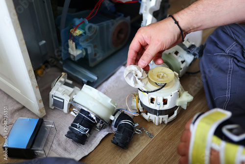Bild auf Leinwand Technician inspecting a damaged dishwasher impeller and pump assembly during appliance repair and maintenance in a modern residential kitchen