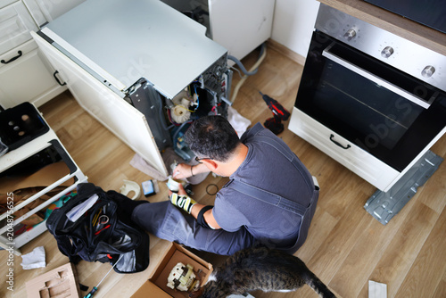 Obraz na płótnie Professional appliance technician repairing a built-in dishwasher in a kitchen,
