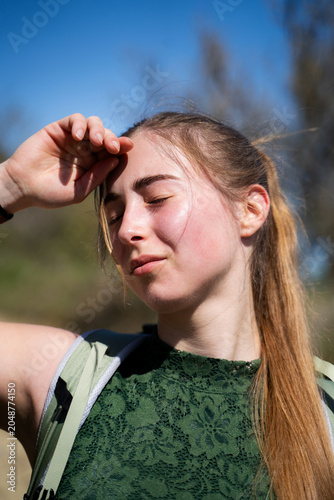 Tableau sur toile Exhausted woman backpacker shielding her face from intense sunlight while outdoors, standing in the sunlight with closed eyes and a tired expression on her faces, close-up portrait
