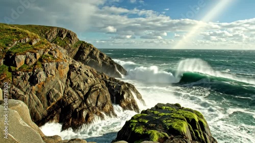 Dramatic ocean waves crashing against jagged coastal cliffs under a bright sun with a vibrant blue sky