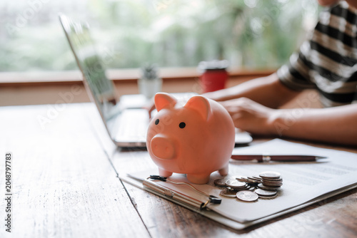 A person deposits coins into a piggy bank beside a laptop and calculator, symbolizing personal finance, saving money, budgeting, financial planning, and wealth management.