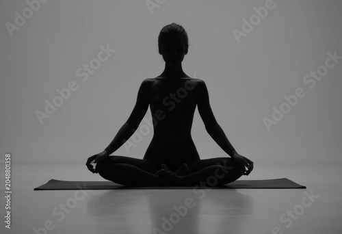 Silhouette of a woman meditating in lotus pose on a yoga mat