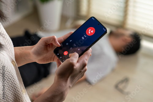 Woman calling emergency service number 112 to aid unconscious man lying on the floor