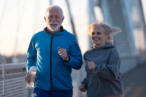 Bild auf Leinwand Happy elderly man and woman exercising outdoors on a pedestrian bridge