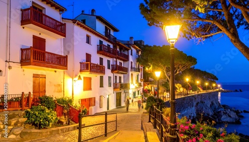 Night scene of seaside village with illuminated buildings, path, and ocean view