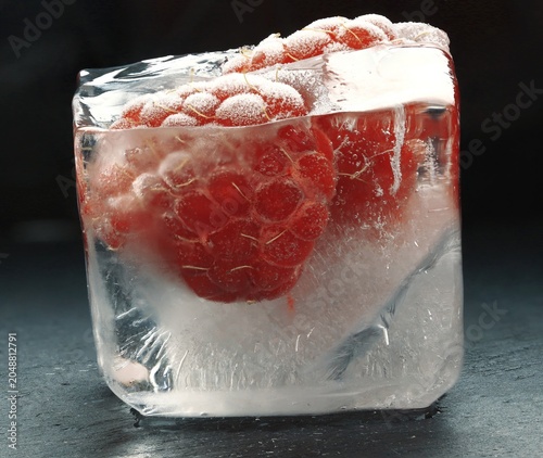 Картината върху платно Frozen raspberries encased in ice cube on dark background