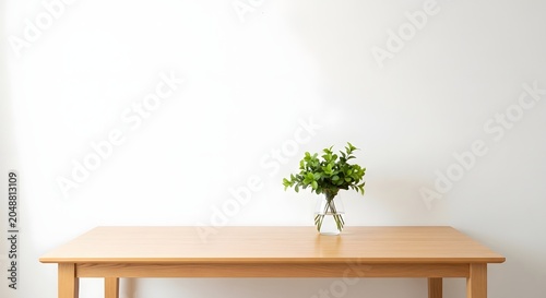 Minimalist interior featuring a green plant in a glass vase on a light wooden table against a white background