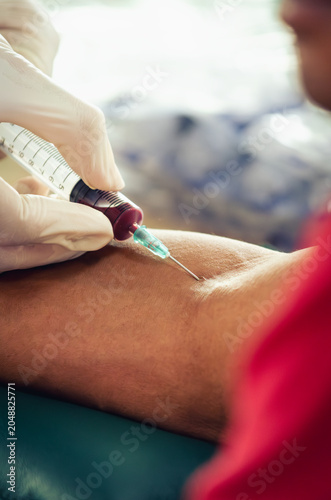 Close up nurse pricking needle syringe in the arm patient drawing blood sample for blood test , Health check