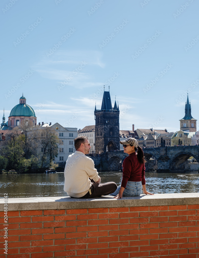 Obraz premium A couple sits peacefully by the Vltava River, enjoying a sunny day in Prague, Czechia