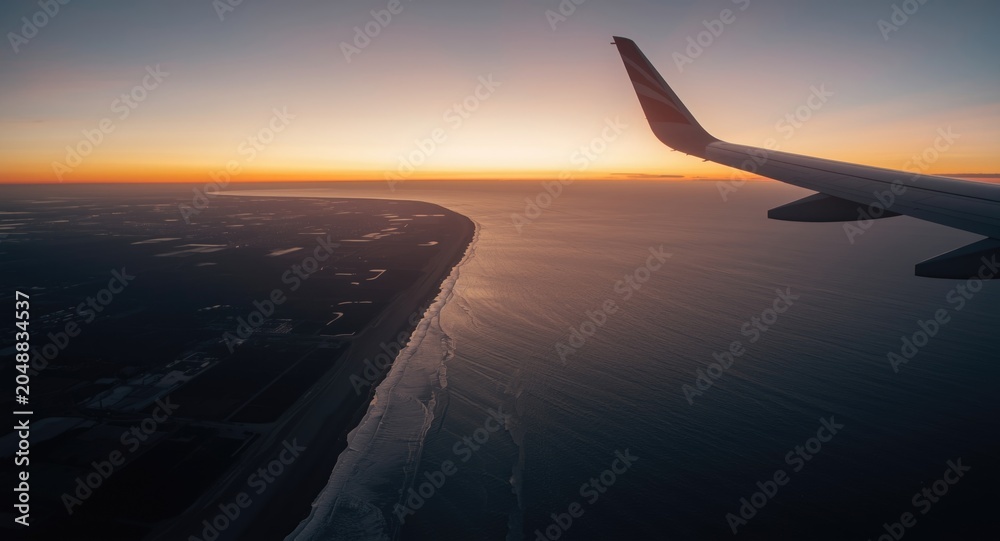 Obraz premium Serene aerial sunset over ocean with sandy coast and airplane wing
