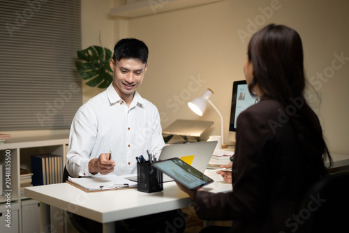 Asian Business Colleagues Meeting at Office Desk with Tablet and Laptop During Evening Work Session