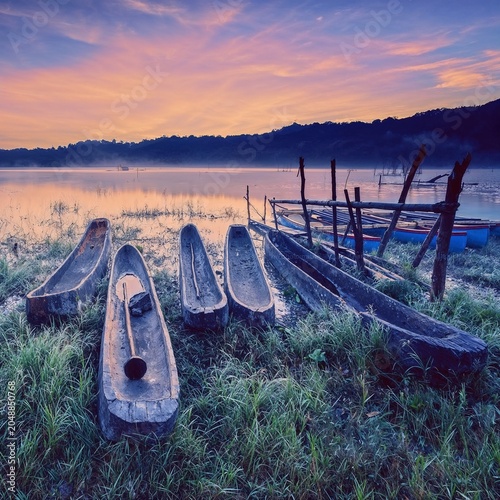 Foto Weathered boats rest along a peaceful lakeshore beneath a glowing sunset sky