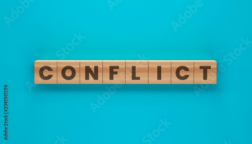 Obraz na płótnie Conflict Wooden Blocks: The word CONFLICT is spelled out on small wooden blocks arranged in a line against a vibrant teal background, symbolizing disagreement and tension